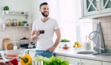 Yakışıklı, gülümseyen, sakallı genç adam fincanından kahve ya da çay içerek evdeki mutfakta dinleniyor.