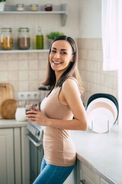 Güzel, gülümseyen, genç esmer kadın hafta sonları harika kahve içer ve evcil mutfakta dinlenir. 