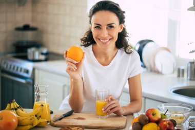 Şirin, güzel ve mutlu esmer kadın mutfakta sebze salatası veya sağlıklı bir içecek hazırlıyor ve eğleniyor.