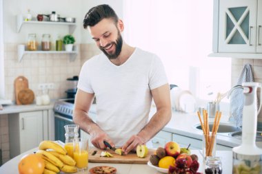 Yakışıklı genç sporcu mutfakta vegan sağlıklı meyve salatası ve smoothie hazırlıyor. Keyfi yerinde.
