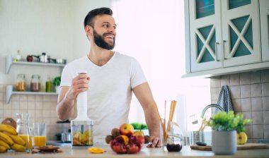 Yakışıklı genç sporcu mutfakta vegan sağlıklı meyve salatası ve smoothie hazırlıyor. Keyfi yerinde.