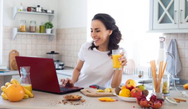 Şirin, güzel ve mutlu esmer kadın mutfakta sebze salatası veya sağlıklı bir içecek hazırlıyor ve eğleniyor.