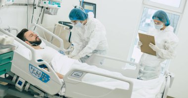 Koruyucu giysili ve maskeli doktorlar, hastane koğuşundaki hasta koronavirüsünü inceliyor.