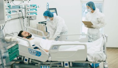 Koruyucu giysili ve maskeli doktorlar, hastane koğuşundaki hasta koronavirüsünü inceliyor.