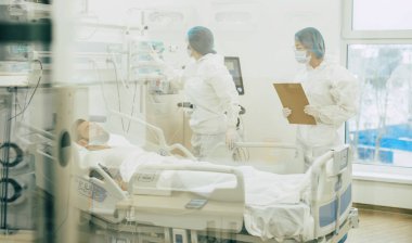 Koruyucu giysili ve maskeli doktorlar, hastane koğuşundaki hasta koronavirüsünü inceliyor.