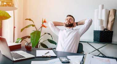 Başarılı, modern sakallı ofis çalışanı çalışma masasında sıkı ve iyi bir çalışmadan sonra dinleniyor.