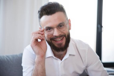 Kendine güvenen, şık, sakallı, gözlüklü ve kanepede otururken resmi olarak şık giyinen iş adamının fotoğrafını çek.