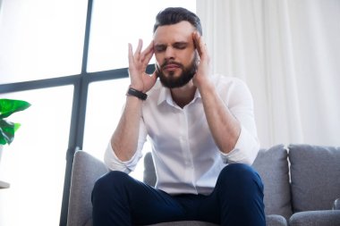 Stresli bir iş adamının başı ağrıyor ve yüzü ağrıyan koltukta oturuyor.