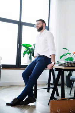 Şık, mutlu, gündelik giyinmiş modern iş adamı kahve molası verirken yeni açılan ofiste poz veriyor.