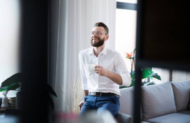 Şık, mutlu, gündelik giyinmiş modern iş adamı kahve molası verirken yeni açılan ofiste poz veriyor.