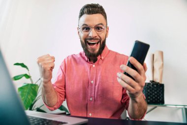 Heyecanlı, mutlu, sakallı, sıradan giyinmiş yakışıklı bir adam, iş, bahis ya da piyangodan dolayı gülümsüyor ve bağırıyor.