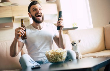 Yakışıklı, heyecanlı, modern sakallı adam TV 'de futbol maçı izlerken kanepede dinleniyor.