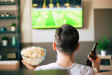 Yakışıklı, heyecanlı, modern sakallı adam TV 'de futbol maçı izlerken kanepede dinleniyor.