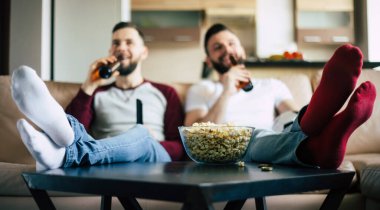 İki genç mutlu sakallı arkadaş, hafta sonu evde kanepede oturup bira içip abur cubur yerken televizyon veya spor maçı izliyorlar.