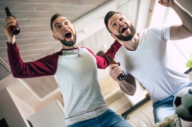 İki en iyi arkadaş ve futbol fanatiği TV 'de maç izleyip, bira içip kanepede takım için tezahürat yaparken atıştırmalık yiyorlar.