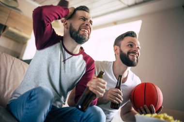 İki heyecanlı genç arkadaş basketbol fanatiği TV maçı izleyip kanepede dinlenirken bağırıyorlar.