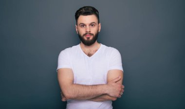 Ciddi ciddi hippi, beyaz tişörtlü modern sakallı adam kameraya bakıyor ve poz veriyor..