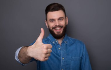 Modern, mutlu, heyecanlı, kot gömlekli, sakallı adam kameraya bakıp eğleniyor.