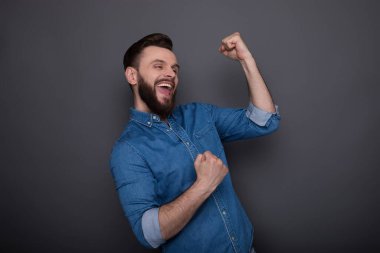 Heyecanlı, sakallı, kot gömlekli adam bağırıyor, kutlama yapıyor ve kazanmak için eğleniyor.