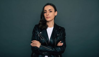 Siyah ceketli sevimli, modern, esmer bayan gri arka planda izole edilmiş kameraya bakıyor.