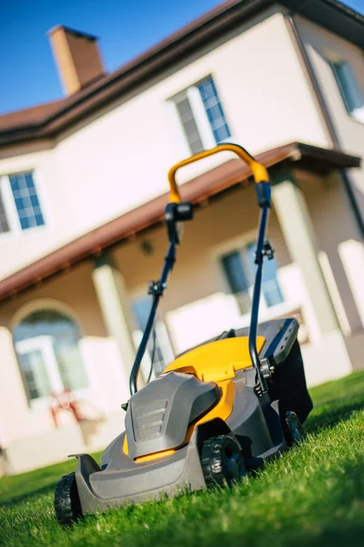 Photo of a modern electric lawn mower standing on a backyard lawn near a house