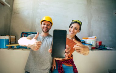 Yeni ev onarımı ya da duvarların yenilenmesi sırasında gündelik giysiler içinde birbirine aşık modern mutlu genç bir çift.