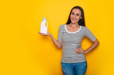 Gündelik giysiler içindeki mutlu genç kız ev temizliği için malzeme ve malzemeyle poz veriyor. 