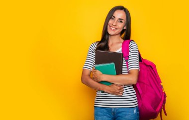 Kitapları ve sırt çantasıyla gülümseyen güzel bir öğrenci kız poz veriyor ve kameraya bakıyor