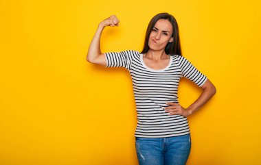 Mutlu sportif güzel ve güçlü kadın sarı arka planda izole edilmiş pazılarını gösteriyor.