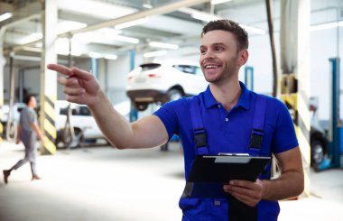 Kendinden emin, genç ve deneyimli araba tamiri uzmanı elinde tabletle arabayı kontrol ediyor ve arıza teşhisi koyuyor.