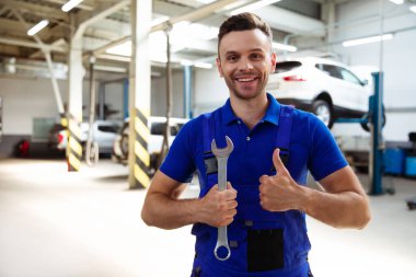 Kendine güvenen genç ve deneyimli araba tamircisi. Araba servisindeki kaldırılmış arabaların geçmişine karşı poz veriyor.