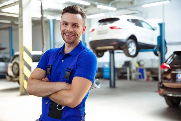Kendine güvenen genç ve deneyimli araba tamircisi. Araba servisindeki kaldırılmış arabaların geçmişine karşı poz veriyor.