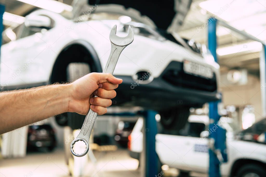 Close up photo of a male auto mechanics hand with an open-end wrench on the background of repairing a car