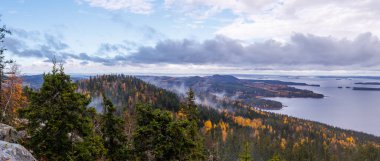 Renkli sonbahar ormanları, sisli tepeler ve dramatik bulutlar altında sakin göl manzaralı İskandinav manzarası kuzey doğasının vahşi ve huzurlu güzelliğini gösteriyor.