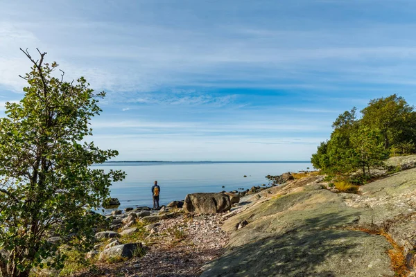 Finlandiya 'da kayalık sahil kayalıkları boyunca yürüyen gezgin, doğa, özgürlük, farkındalık ve macera yolculuğu kavramı ile huzurlu deniz manzarası, turizm ve yaşam tarzı için mükemmeldir.