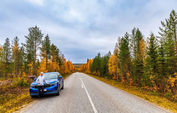 Finlandiya 'da Sonbahar Yolculuğu - Manzaralı orman otoyolunda mavi arabanın yanında duran canlı sonbahar yeşilliği ve karamsar bulutlu gökyüzü, İskandinav manzara seyahat kavramı