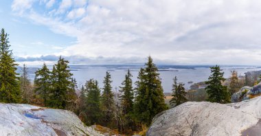 Finlandiya 'daki Koli Ulusal Parkı' nın panoramik manzarası, dramatik bir gökyüzü altında Pielinen Gölü 'nü adalar, çam ormanları ve granit kayalarla gösteriyor. Tam anlamıyla İskandinav doğal güzelliği..