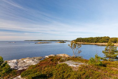 Engebeli granit kayalar, alçak bitki örtüsü ve orman adaları olan sakin İskandinav takımadaları. Berrak, güneşli bir gökyüzünün altında durgun mavi bir su. Kuzey kıyı güzelliği.