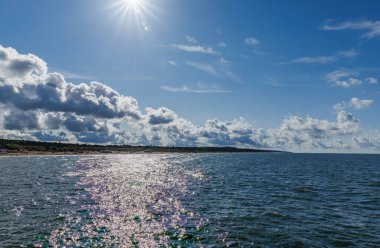 Işıl ışıl deniz suyuyla güneşli kıyı manzarası dramatik bulutlar ve mavi gökyüzü manzaralı okyanus ufku ve sakin yaz sahili manzarası