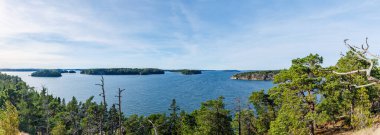 Orman adaları ve berrak gökyüzü altındaki kayalık kıyı şeridi ile gölün manzarası sakin İskandinav doğa manzarası