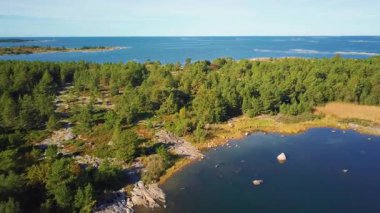 Sonbaharda Finlandiya 'nın kayalık kıyıları, sakin mavi suları ve renkli ormanlarıyla birlikte Baltık takımadaları üzerinde uçan insansız hava aracı görüntüleri. Seyahat, doğa ve manzara teması için ideal