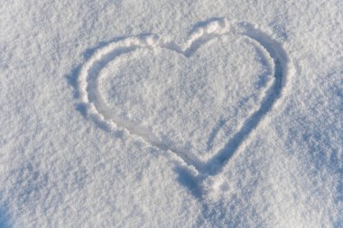 Taze beyaz karla çizilmiş kalp şekli. Aşkı simgeleyen basit ve romantik bir kış sembolü Sevgililer Günü ve karlı bir ortamda huzurlu mevsimsel duygular.