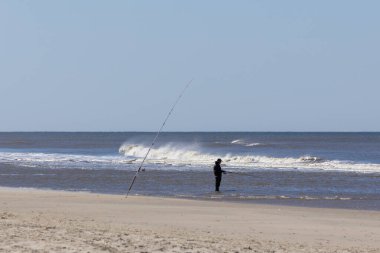 Bir Danimarka sahilindeki kumda dik duran bir olta kamışı ve denizde tanınmayan bir balıkçı vardı. İmaj, İskandinav deniz kıyısında sakin, sabırlı ve sakin bir tatil sağlıyor.