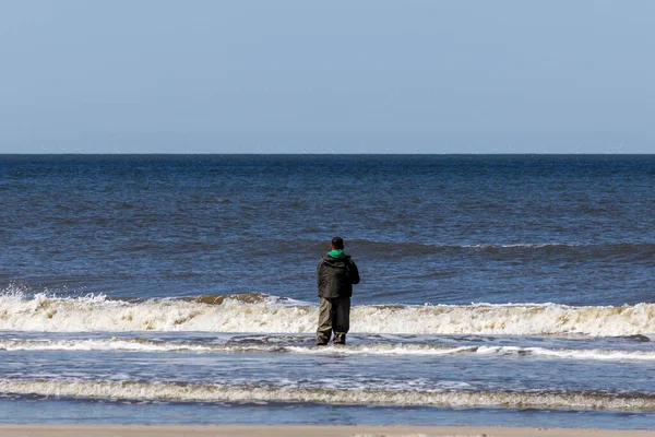 Güneşli bir günde balık tutmaya hazırlanırken denizde duran tanınmamış bir adam. Sakin su ve parlak ışık, sakin bir sahil manzarası yaratıyor. Eğlenceye, yalnızlığa ve boş zamanlara odaklanıyor. Danimarka, Mayıs 2025.