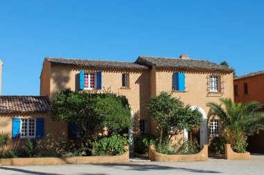 Büyüleyici bir çift geleneksel Portekiz evi, sıcak kum renkli ve canlı mavi pencere panjurları. Binalar klasik terracotta kil çatı kiremitleriyle kaplıyken, ön plandaki yemyeşil ağaçlar güzel bir doğal karşıtlık oluşturuyor.