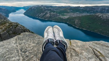 Kürsü Kayası 'nın tepesinde dinlenen adam Preikestolen' de fiyortla güzel Norveç manzarası ve doğası altında, Kürsü Kayası, Norveç