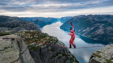 Pulpit Rock, Norveç - Mayıs 2016: Preikestolen, tehlikeli ekstrem spor kavramında ipin üzerinden yürüyen bir adamla güzel Norveç manzarası