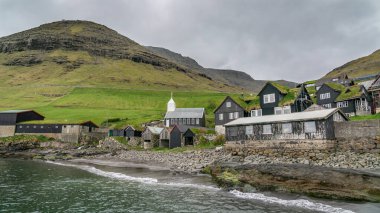 Bour, Faroe Adaları - Ağustos 2019: Yeşil dağlarla çevrili bir fiyorda tepeden bakan tipik bir kuzeyli köy .