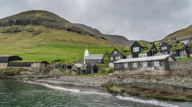 Bour, Faroe Islands - August 2019: Typical nordic village overlooking a fjord surrounded by green mountains . clipart