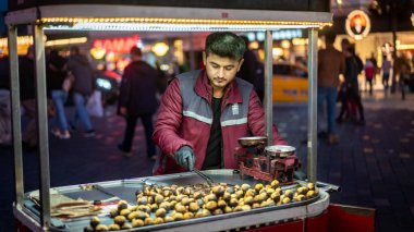 İstanbul, Türkiye - Kasım 2019: Akşam saatlerinde Taksim İstiklal Caddesi 'nde kavrulmuş kestane satan adam. Alan derinliği ve bulanıklaştırma kasıtlı ve orijinal olarak yapılır